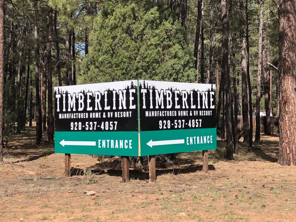 Large black and green entrance sign for Timberline Manufactured Home & RV Resort set among pine trees.