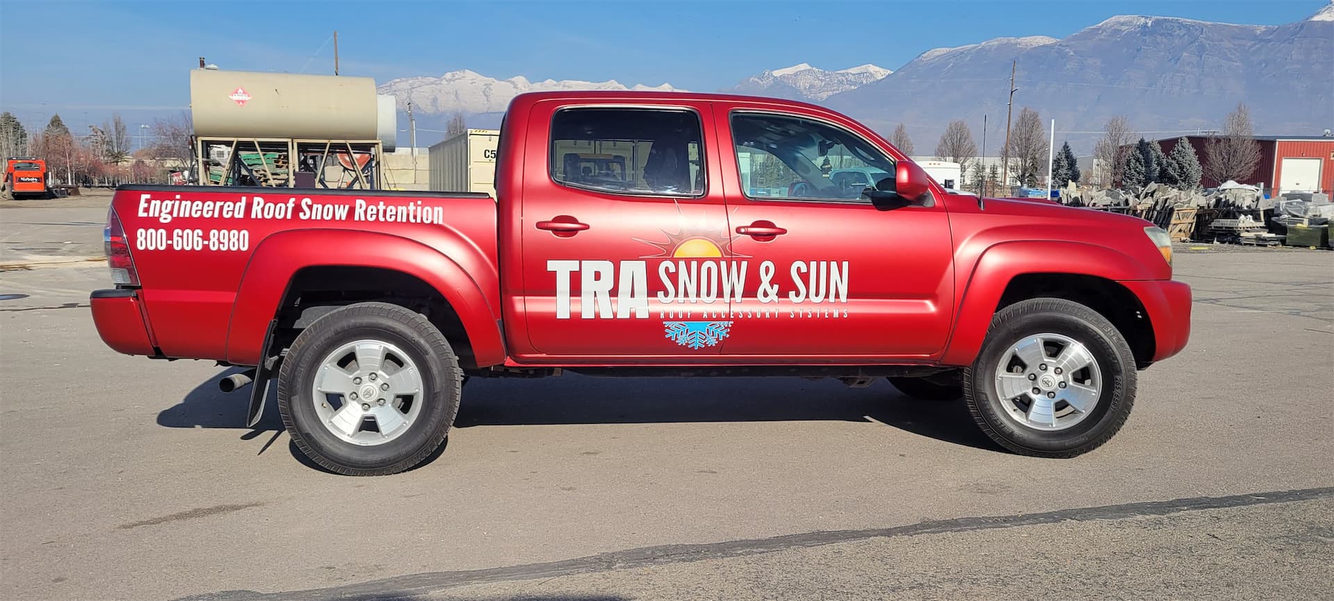 Red pickup truck wrapped with TRA Snow & Sun custom branding decals parked outdoors.
