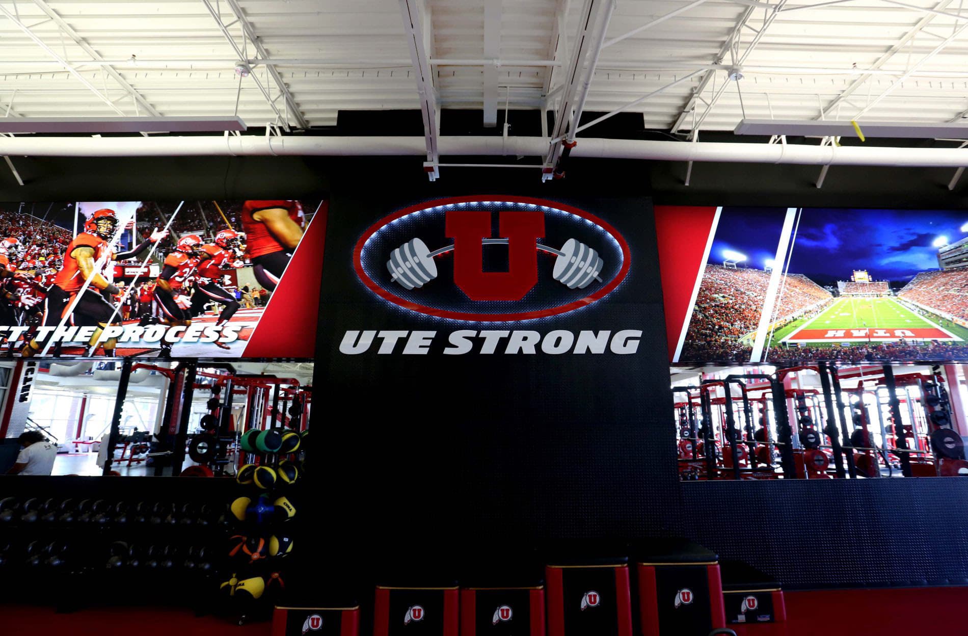 Interior of an athletic weight room featuring Ute Strong illuminated wall signage and large football action graphics.