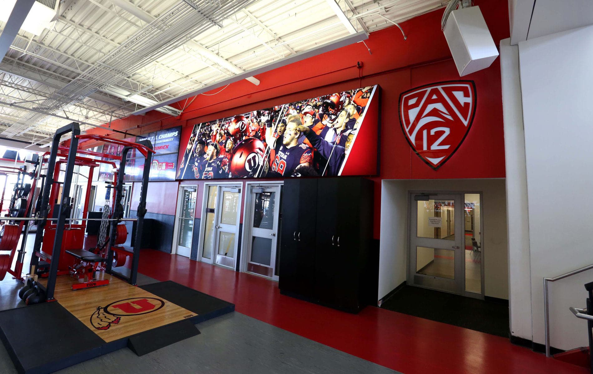 Interior view of a university weight room with custom red wall graphics, Pac-12 logo, and illuminated display wall.