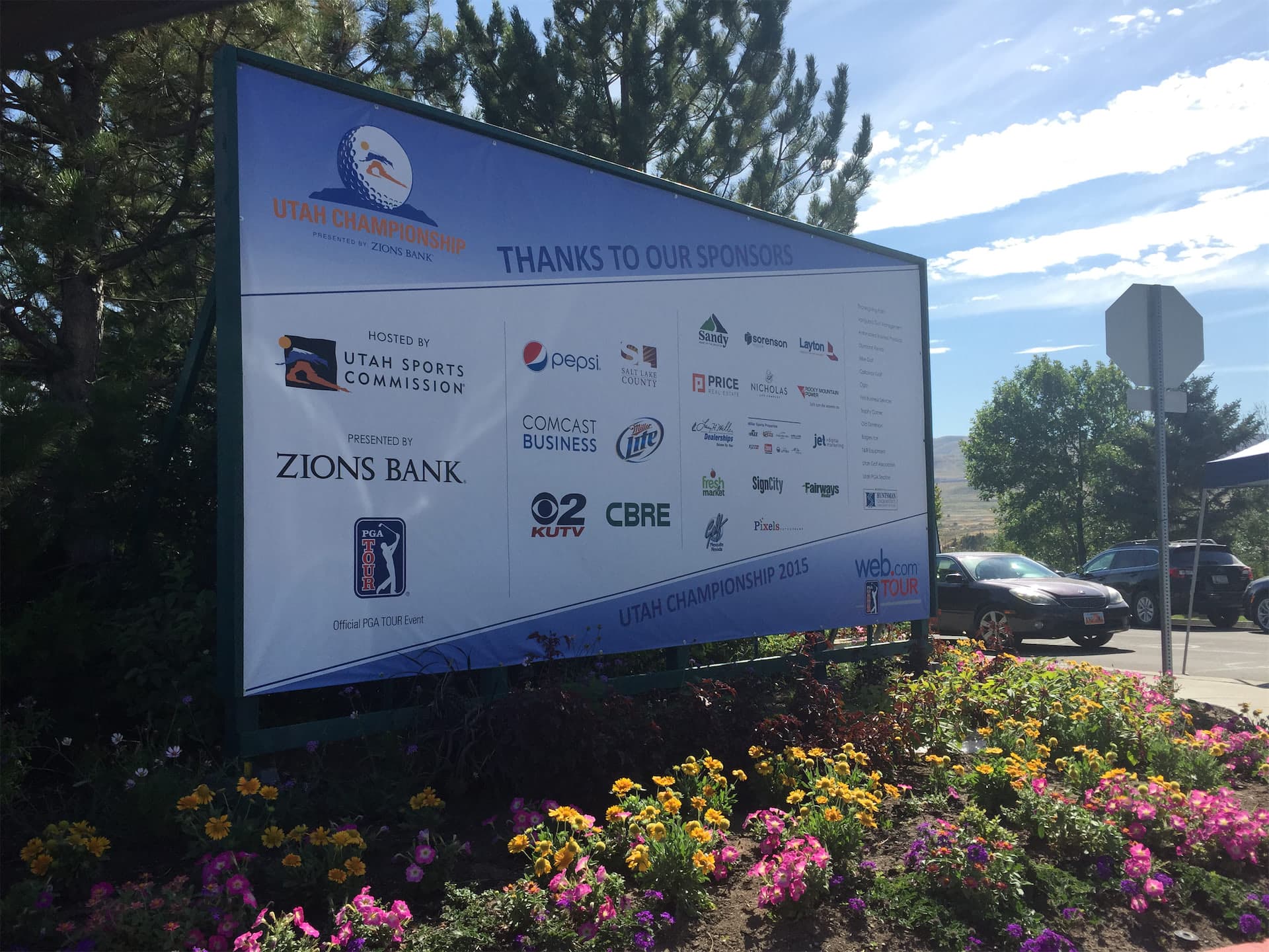 Large outdoor sponsor sign for the 2015 Utah Championship golf tournament surrounded by colorful flower beds.