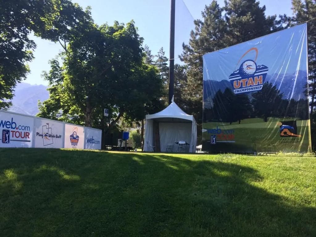 Large Utah Championship banner and event signage on a golf course near a white event tent.