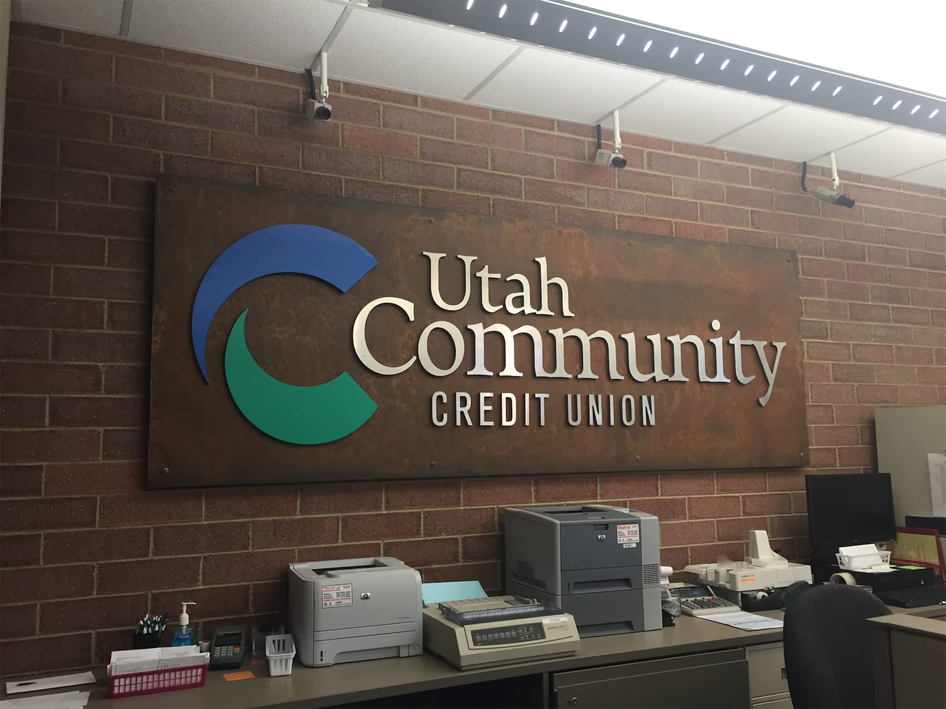 Utah Community Credit Union metal wall sign with logo mounted on a brick lobby wall.