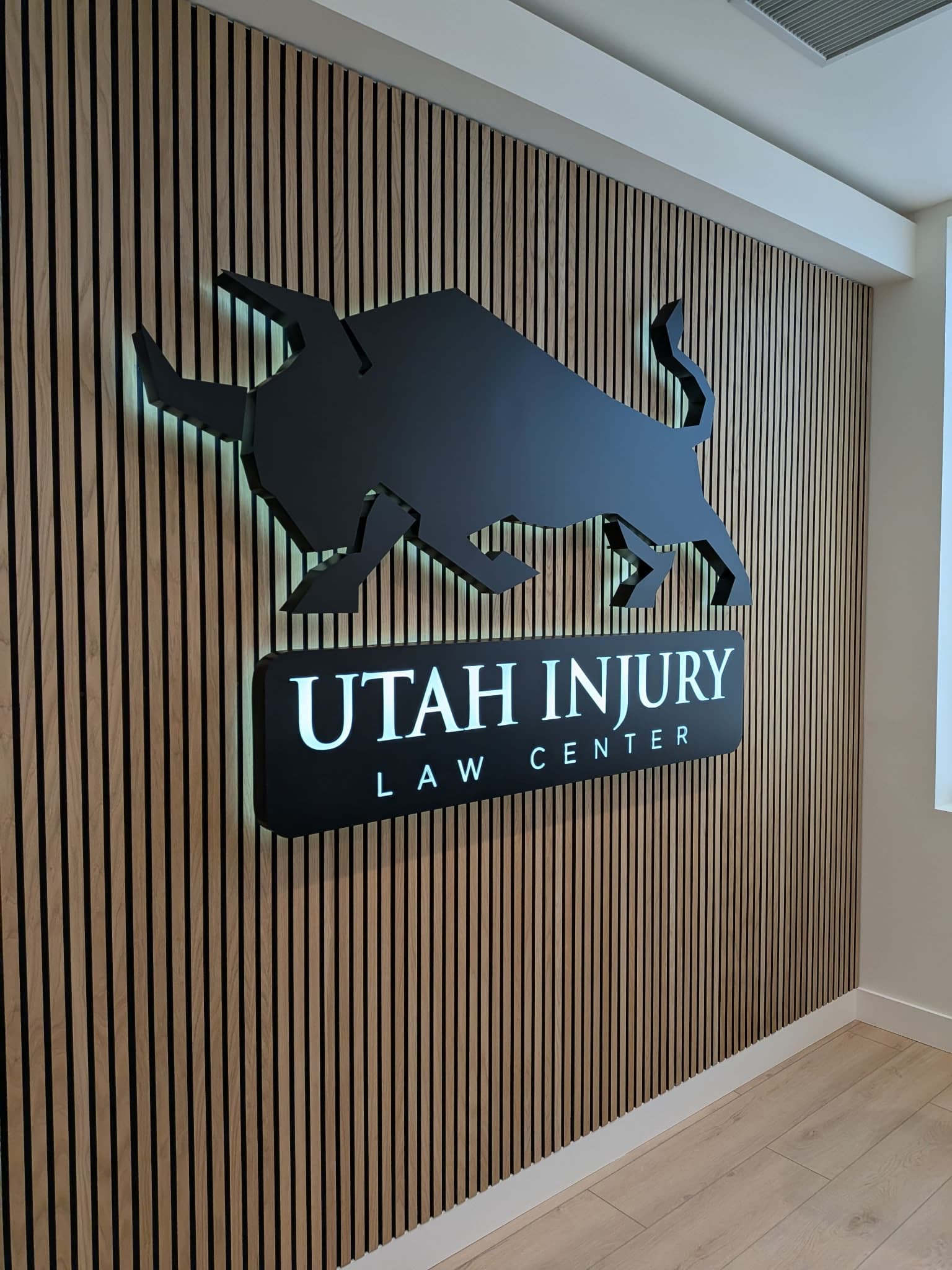 Backlit 3D lobby sign for Utah Injury Law Center mounted on a modern wood slat wall.