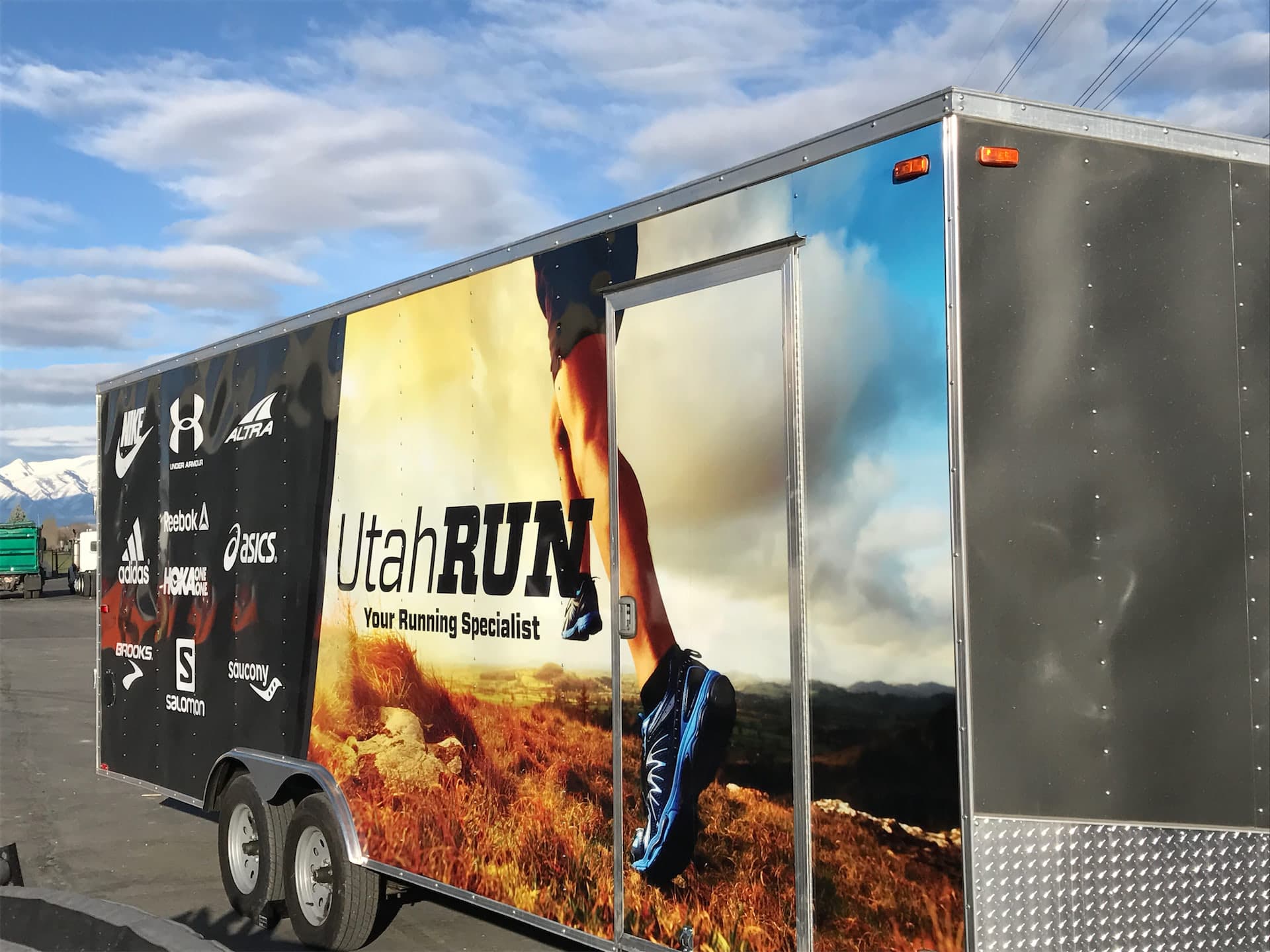 Custom vinyl graphics wrap on a Utah Run cargo trailer featuring running shoe brand logos.