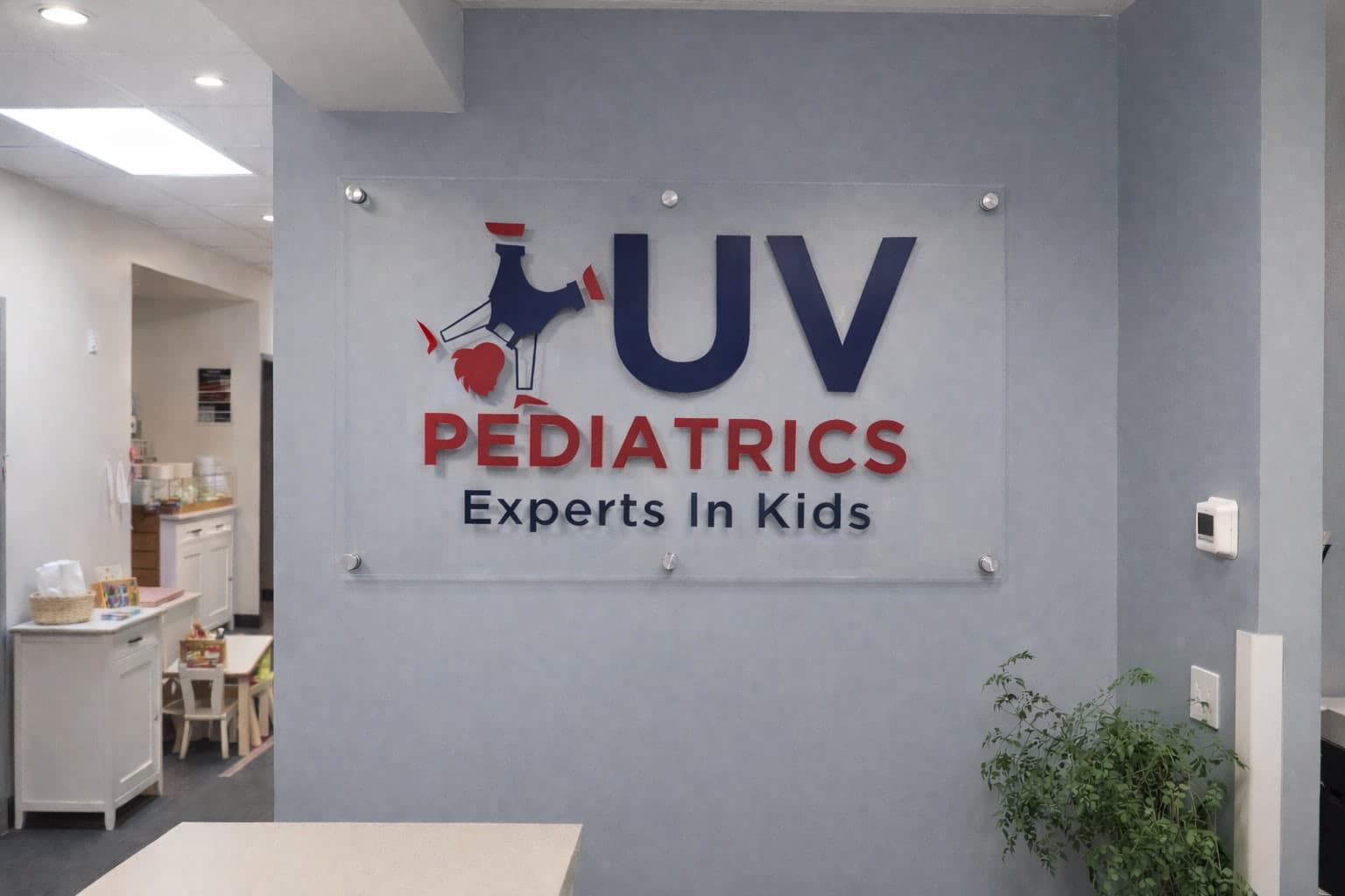 Acrylic lobby sign mounted on a light blue wall for UV Pediatrics Experts In Kids.