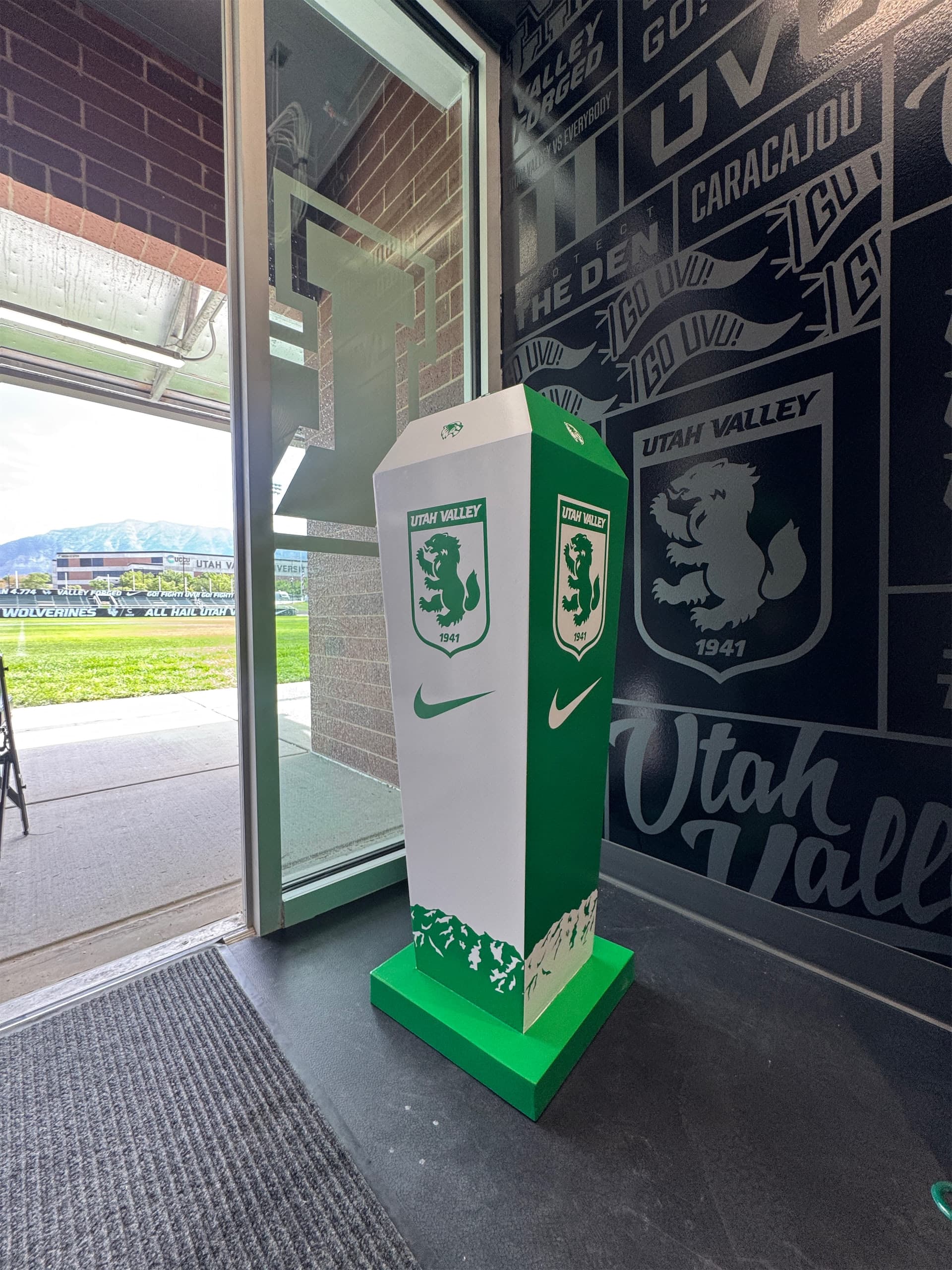 Branded green and white Utah Valley University podium stand next to custom wall graphics inside an athletic facility.