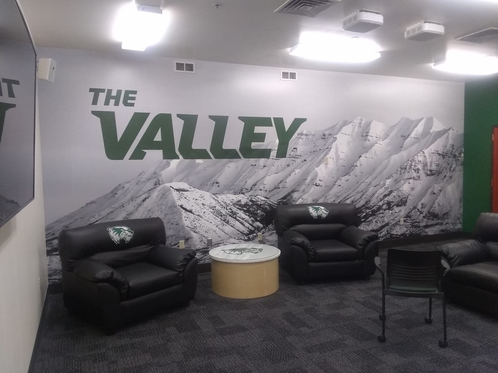 Utah Valley University lounge area with custom mountain wall mural featuring 'THE VALLEY' text and branded armchairs.