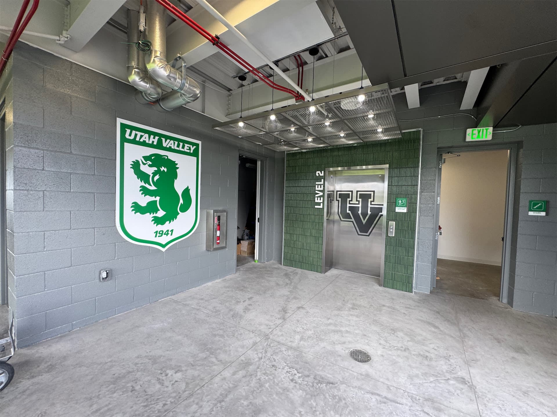Utah Valley University branded elevator hallway with green wolverine shield wall graphic and UV logo on elevator doors.