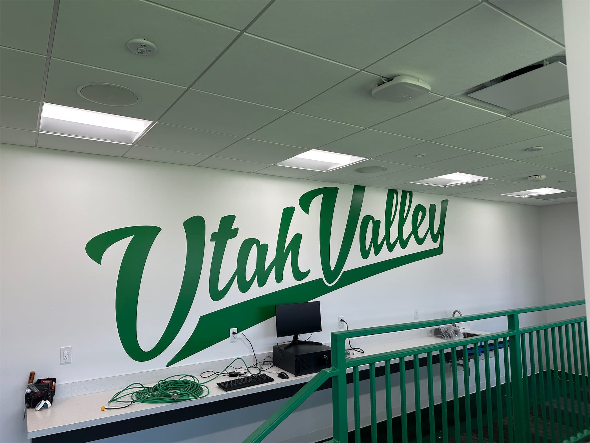 Large green Utah Valley script wall decal installed on a white interior wall in a sports or facility area.