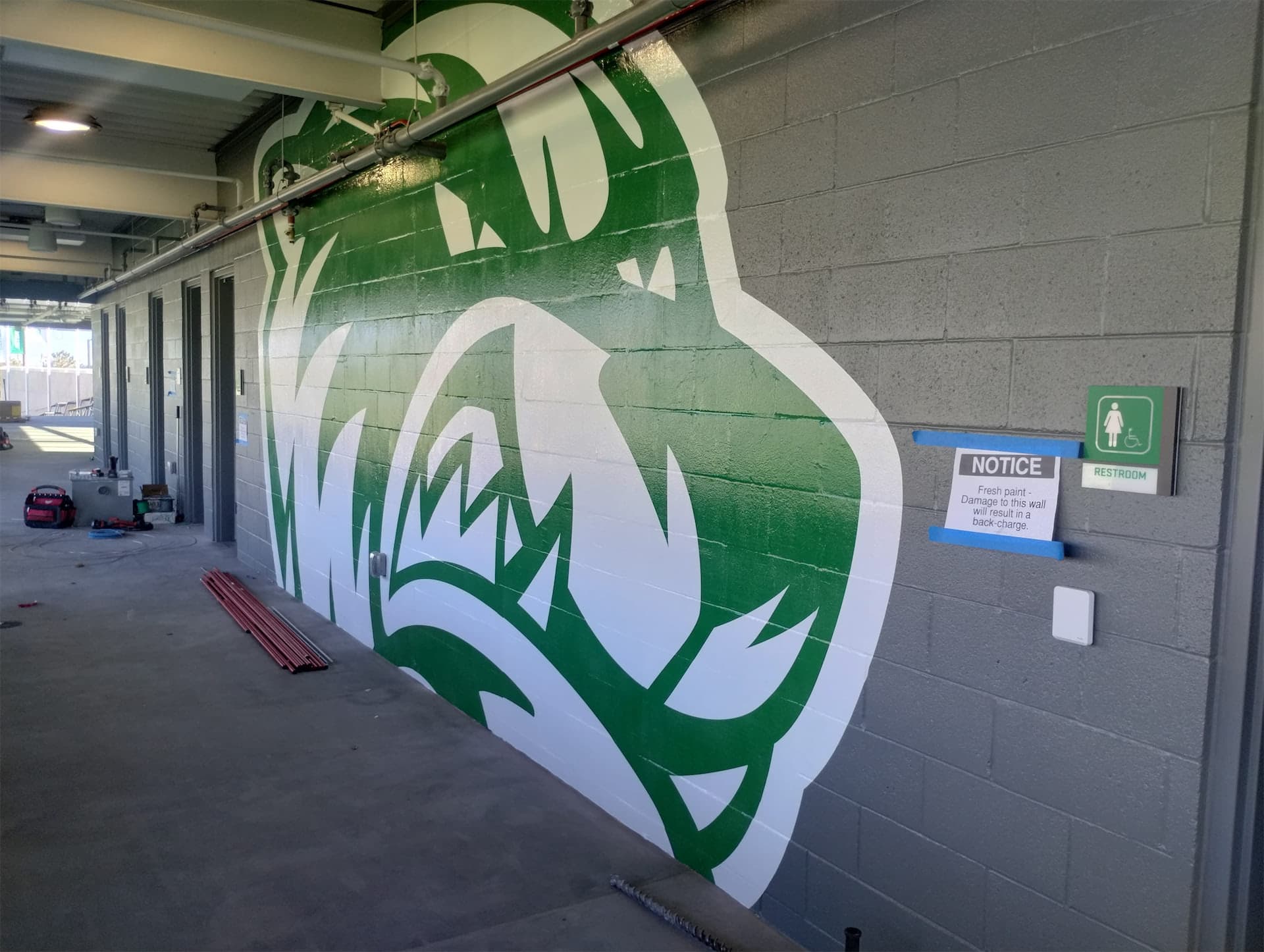 A large green and white UVU wolverine graphic painted on a grey cinder block wall in a building concourse.