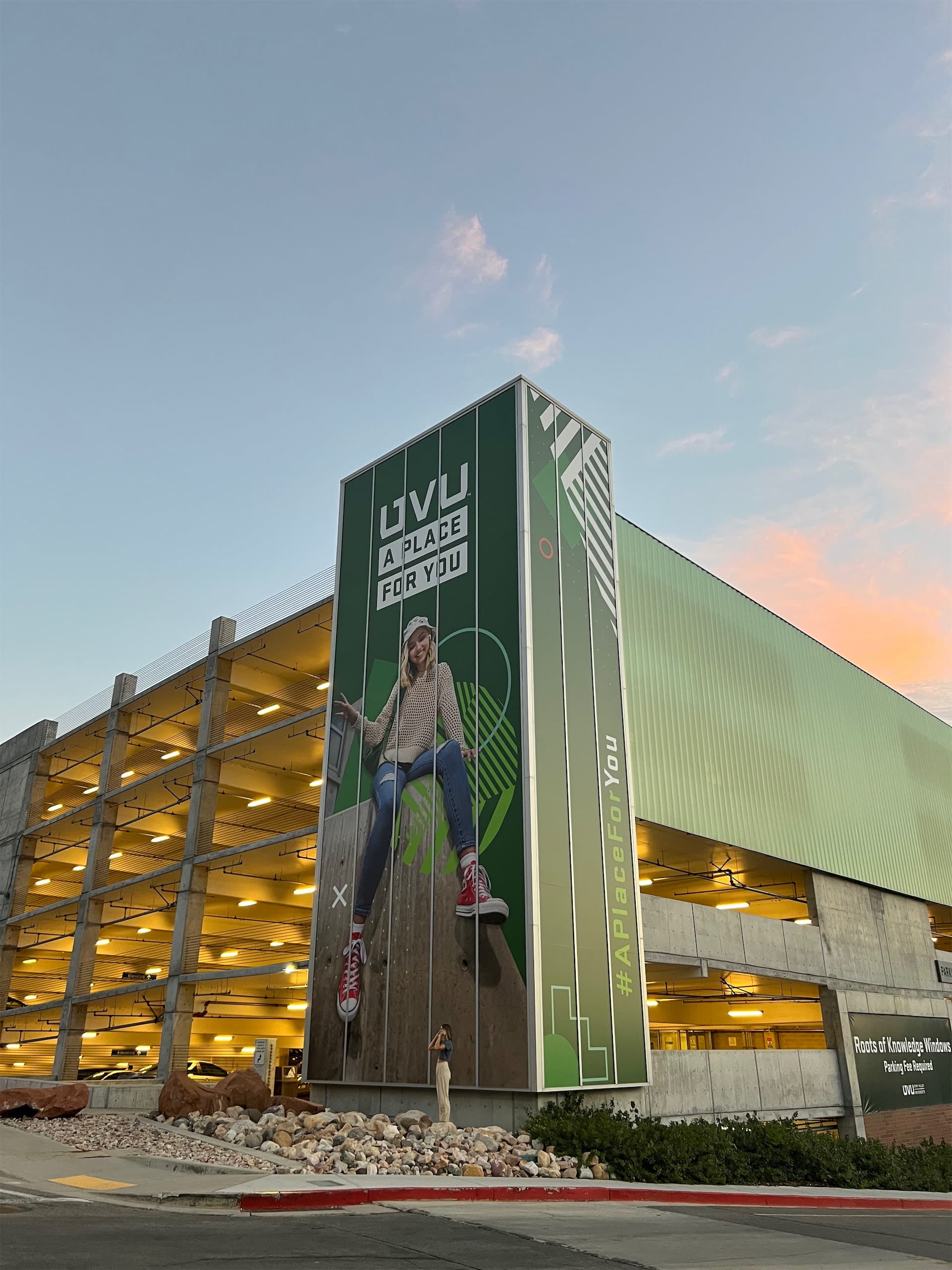 Large UVU building wrap on a campus parking garage displaying the text 'UVU A Place For You'.