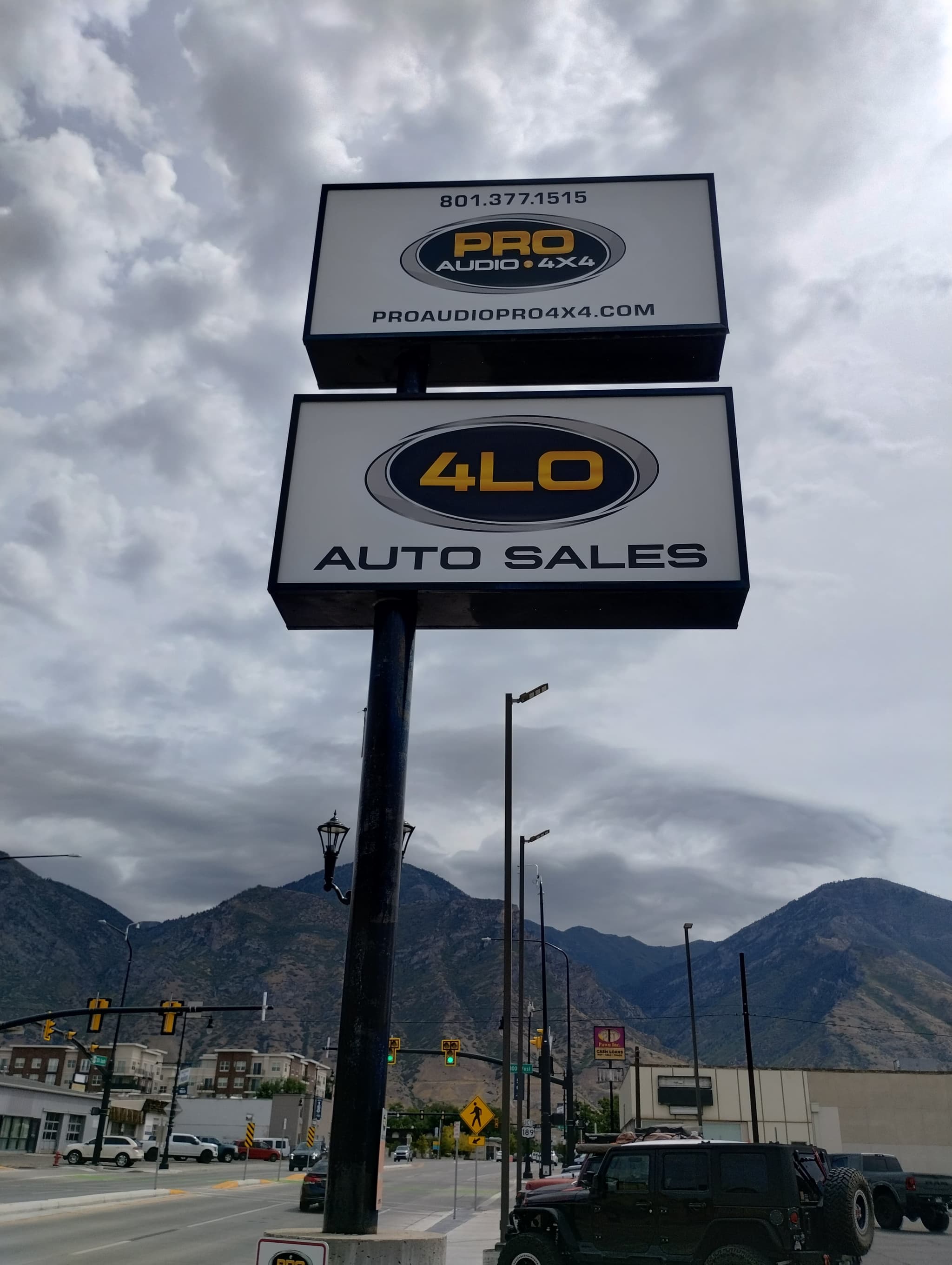Double-sided illuminated pole sign for Pro Audio 4x4 and 4LO Auto Sales with mountains in the background.