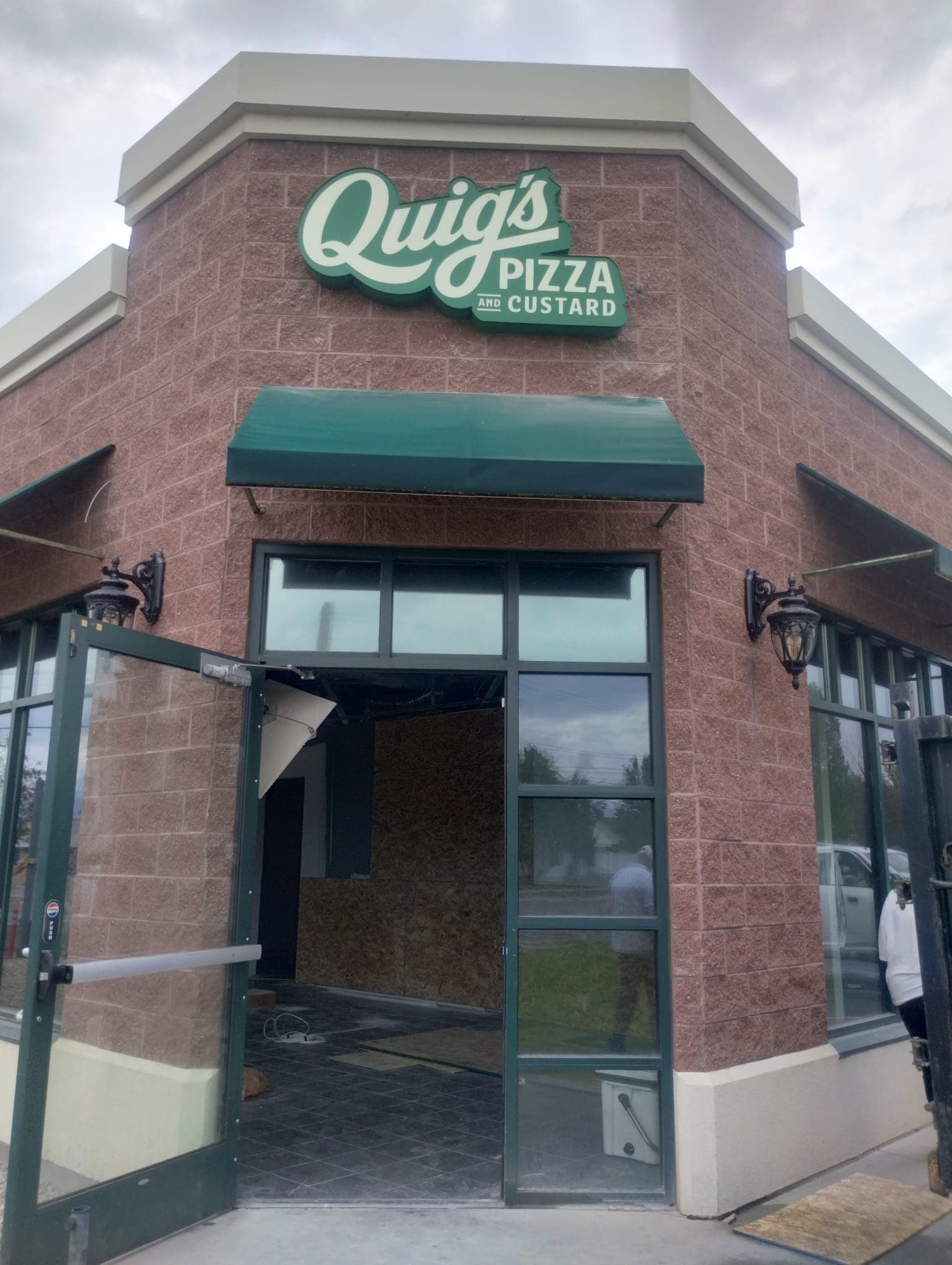 Green and white Quig's Pizza and Custard exterior sign mounted on a red brick storefront.