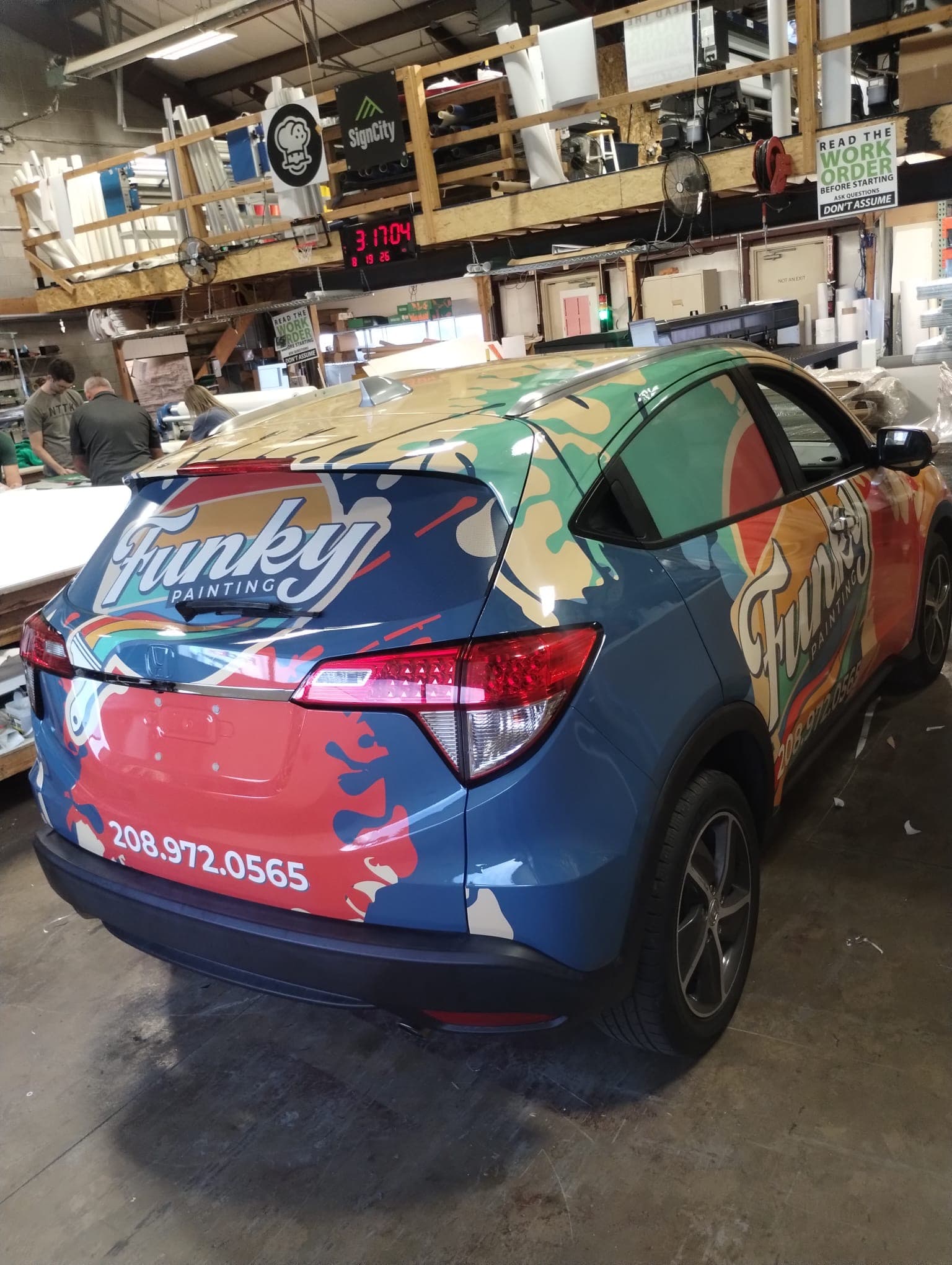 Colorful custom vehicle wrap for Funky Painting on a Honda SUV inside a wrap shop.