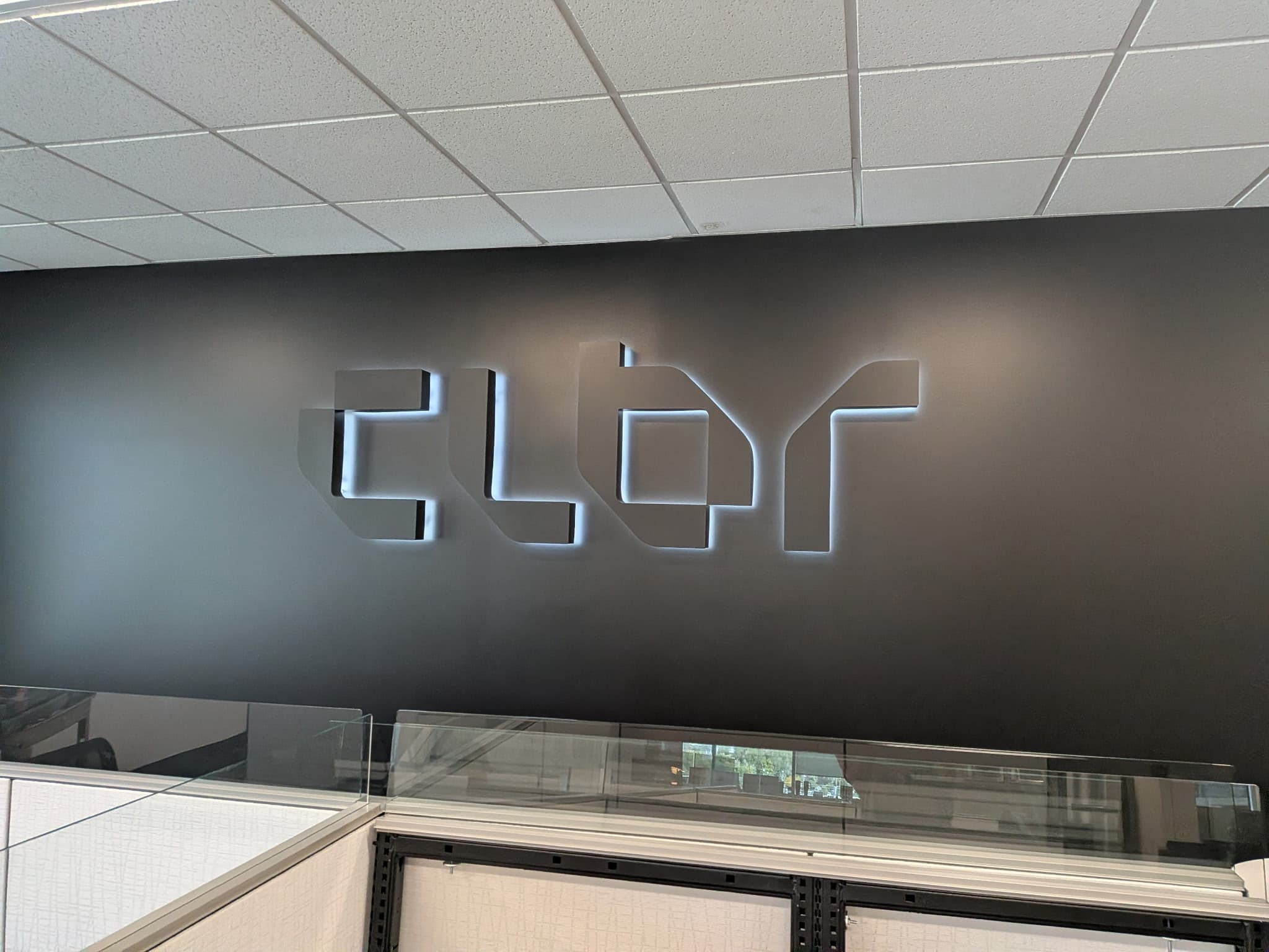 Illuminated backlit dimensional logo sign mounted on a dark matte office wall.